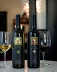 Two wine bottles with labels and two glasses of wine on a table.