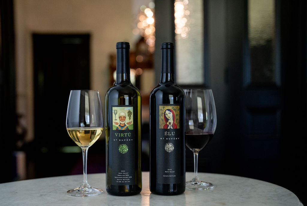 Two wine bottles with labels and two glasses of wine on a table.