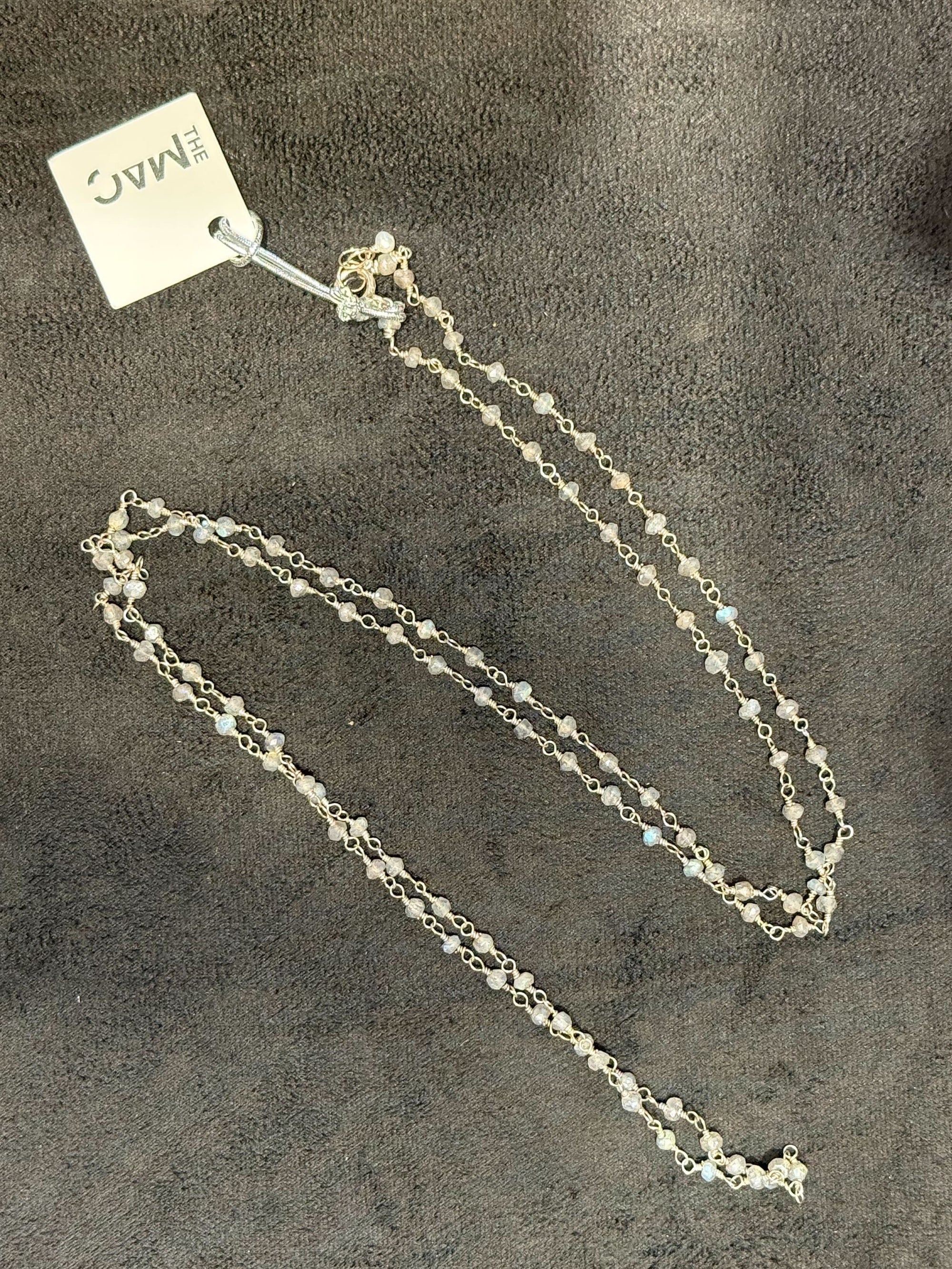 Silver necklace on a textured gray surface with a visible brand tag.