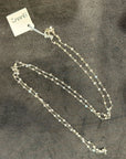 Silver necklace on a textured gray surface with a visible brand tag.